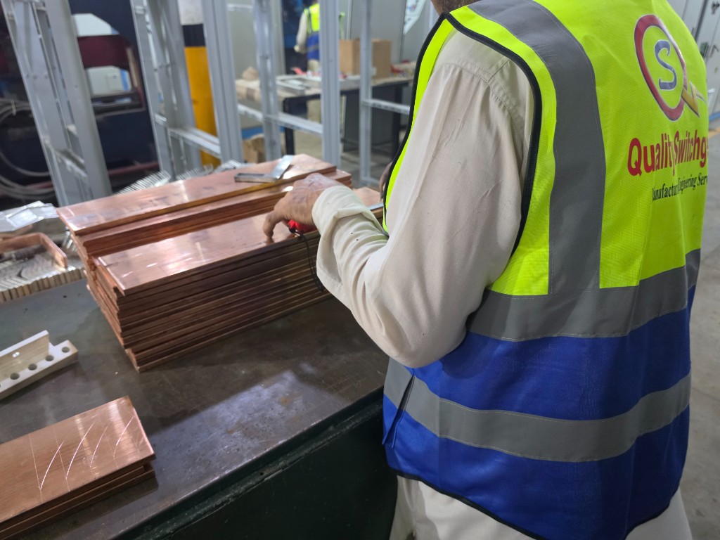 Technician measuring copper busbars on the fabrication bench